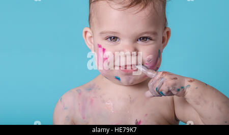 Divertente sorriso di un simpatico baby Girl coperto di vernice Foto Stock