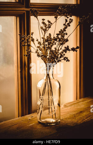 Mazzo di fiori secchi di fiori di campo in un vintage vaso di vetro su un vecchio tavolo di legno da una finestra in stile georgiano, tonica Foto Stock