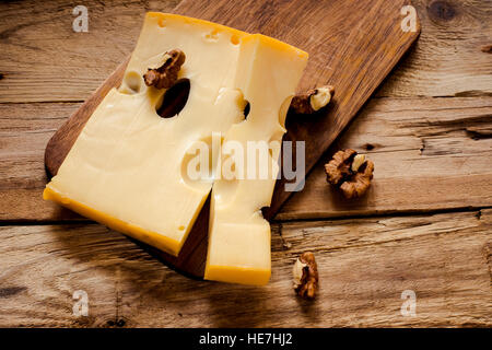 Maasdam cavernoso formaggio al buio su un tagliere con dadi vista dall'alto, il fuoco selettivo Foto Stock