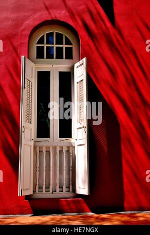 Parete rossa con finestra e persiane bianche Foto Stock
