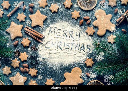Buon Natale saluto scritto sulla farina sulla lavagna. Telaio con gingerbread stelle cookie, gingerbread man cookies e spezie Foto Stock