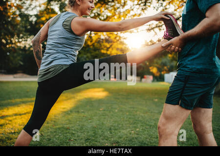 Montare la giovane donna facendo esercizi di stretching con l aiuto di un personal trainer nel parco. Azienda di pullman gamba della femmina. Foto Stock