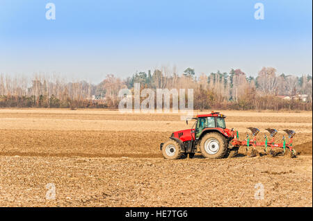 Manodopera agricola, Trattore rosso arando un campo Foto Stock