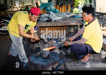 Ajam Kor Neekow e sua fabbri / bladesmiths facendo una spada tradizionali a loro forge in Lampang, Thailandia Foto Stock
