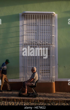 Disabilitato uomo su una mobilità scooter passando un tipico ferro finestra bloccato sulla strada in Trinidad, Cuba Foto Stock