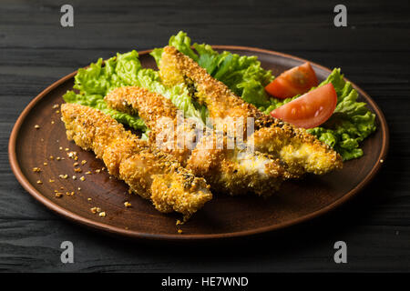 Pesce fritto con lattuga e pomodoro su tavoli in legno nero Foto Stock
