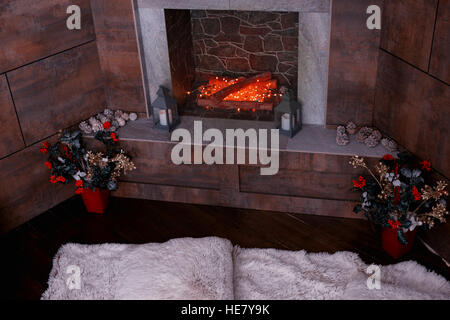 Decorate caminetto moderno con candele, fir-coni nella stanza vivente con bianco tappeto peloso e vasi con fiori artificiali Foto Stock