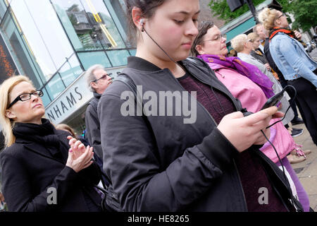 Una giovane donna ascolta musica sul suo telefono cellulare mentre aspettano il traffico di segnali per modificare per consentire la sua per attraversare la strada. Foto Stock