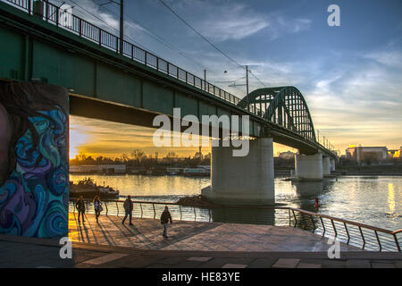 Belgrado, Serbia - Walkers su una passeggiata sotto il tram ponte che attraversa il fiume Sava al crepuscolo Foto Stock