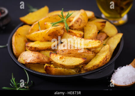 Ruddy patate al forno cunei con rosmarino e aglio su uno sfondo scuro. Foto Stock