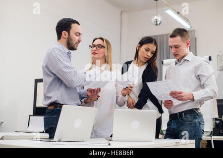 Il gruppo di quattro diversi uomini e donne in abbigliamento casual parlando in ufficio Foto Stock