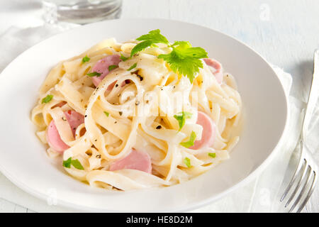 Alfredo tagliatelle con salsicce e verdi su piastra bianca - fatti in casa pasta cremosa Foto Stock