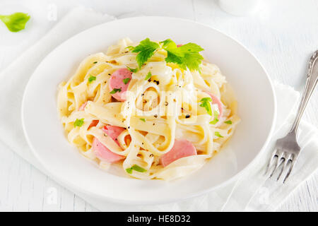 Alfredo tagliatelle con salsicce e verdi su piastra bianca - fatti in casa pasta cremosa Foto Stock