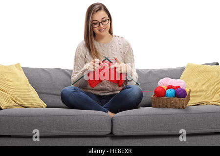 Felice giovane donna seduta su un divano e maglia isolati su sfondo bianco Foto Stock