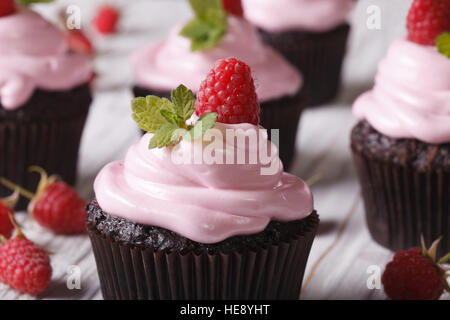 Gustosa pasticceria: tortini di cioccolato con crema rosa e lampone sulla tavola di close-up orizzontale. Foto Stock