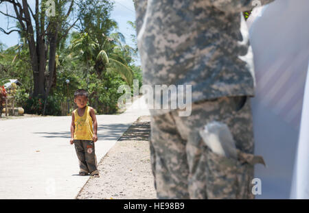 Un bambino filippino di orologi come Stati Uniti Army Spc. Edward Shipp, Distacco 1230 operazioni psicologiche specialista, 324324le Operazioni psicologiche (PSYOP) azienda, Distacco 1230 PSYOP Specialista, aiuta i membri della comunità di un barangay, o villaggio, post un esercizio Balikatan 2015 banner lungo una recinzione, 23 aprile in Bahile, PALAWAN FILIPPINE. Shipp è una parte della BK15 Informazioni militari azioni di sostegno e viaggi di barangays per informare i membri della comunità circa BK15 e rafforzare le relazioni con le Filippine. Quest anno segna il 31 iterazione dell'esercizio, che è un annuale Foto Stock