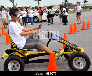 Nobuki Alex, da un Okinawense foster home, cerca un 'Drink Buster' bike intorno a coni indossando occhiali ubriaco durante il funzionamento Sakura sul Kadena Air Base, Giappone, 28 marzo 2014. Per tutto il giorno, i bambini hanno dato dimostrazioni di HH-60 Pave hawk pararescueman, militari cane da lavoro dei gestori, e ordinanza sugli esplosivi smaltimento aviatori, e furono i partecipanti durante il campo eventi. Naoto Anazawa) Foto Stock