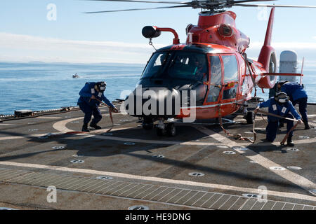 Il suo equipaggio a bordo del guardacoste Midgett, un 378-piede alto-endurance homeported fresa a Seattle, collegare le cinghie di ancoraggio ad un MH-65 Delfino elicottero dalla stazione aria Port Angeles, nello Stato di Washington, dopo essere atterrato sul ponte di volo dell'Midgett durante il corso di formazione in stretto di Juan de Fuca, 13 ottobre, 2015. Entrambi i membri dell'equipaggio dalla fresa e stazione di aria ha beneficiato della formazione in corso opportunità. (U.S. Coast Guard Petty Officer 1. Classe Levi leggere) Foto Stock