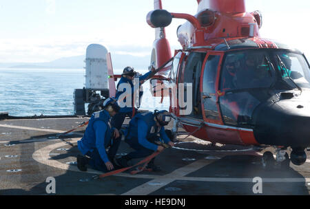 Il suo equipaggio a bordo del guardacoste Midgett, un 378-piede alto-endurance homeported fresa a Seattle, collegare le cinghie di ancoraggio ad un MH-65 Delfino elicottero dalla stazione aria Port Angeles, nello Stato di Washington, dopo essere atterrato sul ponte di volo dell'Midgett durante il corso di formazione in stretto di Juan de Fuca, 13 ottobre, 2015. Entrambi i membri dell'equipaggio dalla fresa e stazione di aria ha beneficiato della formazione in corso opportunità. (U.S. Coast Guard Petty Officer 1. Classe Levi leggere) Foto Stock