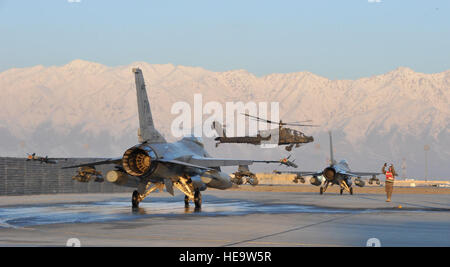 Una coppia di stati uniti Air Force F-16 Fighting Falcons preparare al servizio taxi fuori per la pista mentre un U.S. Esercito AH-64 elicottero Apache vola passato a Bagram Air Field, Afghanistan, 11 febbraio, 2014. Entrambi i tipi di aeromobili sono utilizzati per il supporto delle operazioni di terra in Afghanistan. Senior Master Sgt. Gary J. Rihn Foto Stock