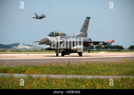 Un 35th Fighter Squadron F-16 Fighting Falcon taxi sulla Kunsan Air Base pista come un 80th Fighter Squadron F-16 Fighting Falcon decolla durante l'esercizio Buddy Wing 15-4 a Kunsan Air Base, Repubblica di Corea, 16 luglio 2015. I cinque giorni di trimestrale di prontezza operativa esercizio migliorata funzionalità strategica a Kunsan generando combattere airpower in una simulazione di chimica, biologica, radiologica, nucleare e ad alta resa ambiente esplosivo. (U.S. Air Force foto di Senior Airman Katrina Heikkinen/rilasciato) Foto Stock