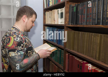 Un uomo con una barba sceglie un libro in biblioteca. Foto Stock