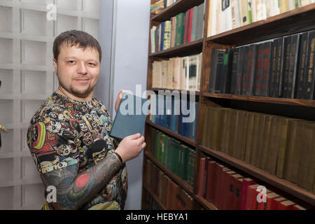 Un uomo con una barba sceglie un libro in biblioteca. Foto Stock