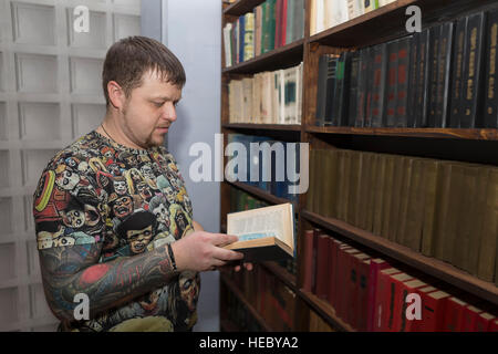 Un uomo con una barba sceglie un libro in biblioteca. Foto Stock
