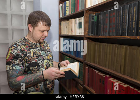 Un uomo con una barba sceglie un libro in biblioteca. Foto Stock