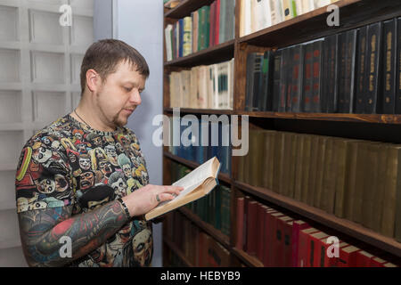 Un uomo con una barba sceglie un libro in biblioteca. Foto Stock