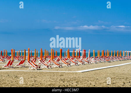 Arancione vuota di ombrelloni e sdraio in spiaggia Foto Stock