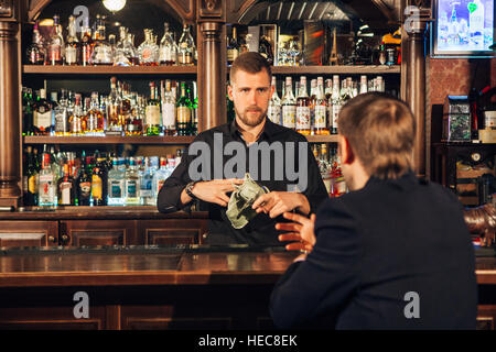 Sorridente attraente giovane barista tergi bicchieri e a parlare con l'uomo in bar Foto Stock