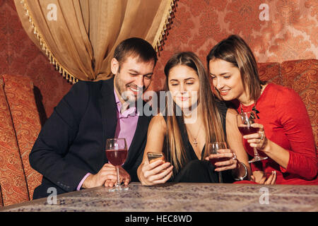 Carino due donne e un uomo seduto nel ristorante utilizzare il telefono Foto Stock