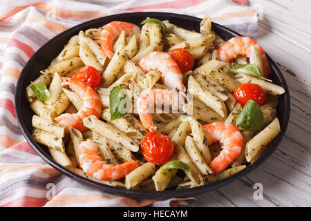 Penne pasta con gamberetti, pomodoro e pesto closeup su una piastra orizzontale. Foto Stock