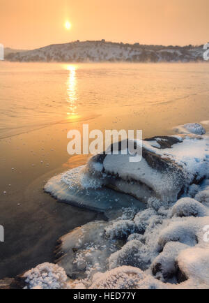 Winter landscape with snowy stones at the beautiful river at sunset. Christmas background. Colorful rural landscape Foto Stock
