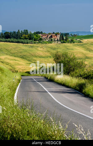 Verde tipico paesaggio toscano in Val d'Orcia con colline, un piccolo villaggio, Campi, alberi, una strada tortuosa e cielo molto nuvoloso Foto Stock