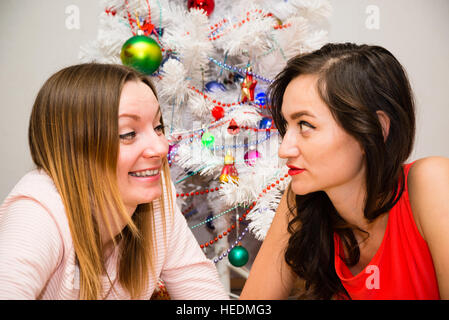 Natale, sorridente due giovani ragazze che giace sul tappeto in background di un albero di Natale illuminato Foto Stock