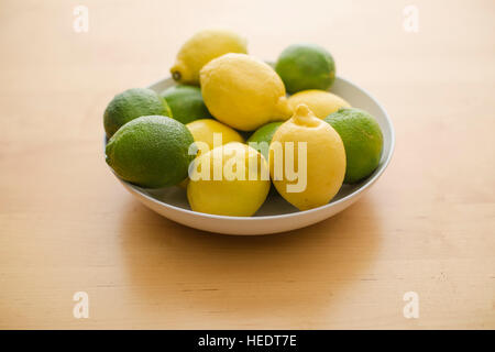 Un grappolo di limoni e limette ammucchiati in una ciotola bianco. Foto Stock