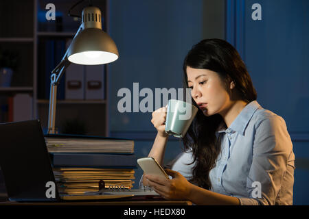 Asian business donna parlare sullo smartphone lavoro straordinario tarda notte. in ambienti chiusi sullo sfondo di office Foto Stock