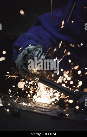 Metallo angolo del lavoratore la rettifica di un pezzo di acciaio. La formazione di scintille da taglio di volare ovunque. Foto Stock