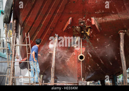 Un uomo che lavora sulla rondella di pressione per la pulizia scafo cirripedi antivegetativo e alghe marine al porto Foto Stock