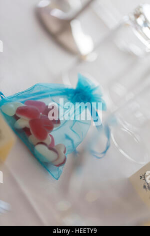 Tavolo per la cena insieme per la celebrazione dei matrimoni con gli occhiali e il blu organza rigata del rosso e del bianco cuore caramelle Foto Stock