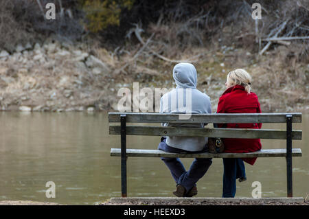 Una giovane coppia seduta su una panchina nel parco in autunno con le spalle alla telecamera. Foto Stock