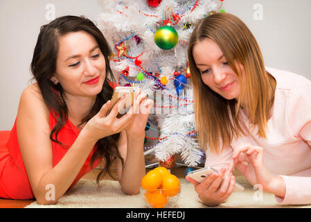 Natale, sorridente due giovani ragazze che giace sul tappeto in background di un albero di Natale illuminato Foto Stock