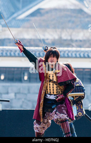 Yosakoi giapponese festival. Danzatori vestiti come il samurai warriors, esecuzione di breve mostra sul palco con il Castello di Kumamoto in background. Foto Stock