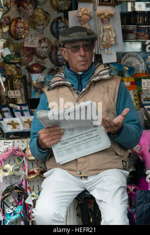 Uomo seduto al negozio di souvenir leggendo un giornale, Venezia, Veneto, Italia Foto Stock