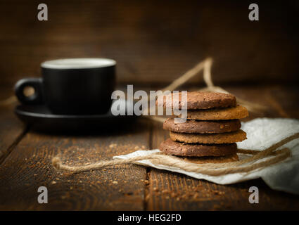 Biscotti impilati sul legno scuro dello sfondo con tazza di caffè. Foto Stock