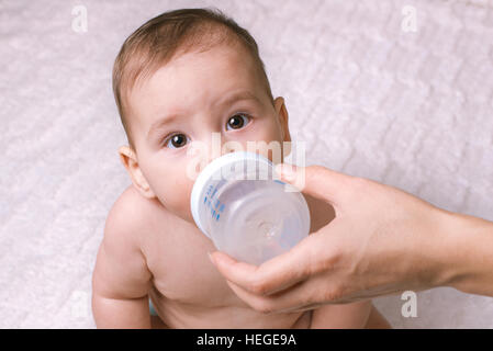 Carino piccolo bambino essendo alimentato da una bottiglia con lo sguardo in alto al di sopra della parte superiore alla fotocamera con ampia eyed curiosità Foto Stock