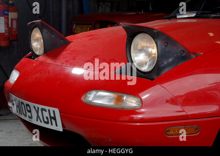 Pop up fari anteriori su un rosso Mazda MX5 auto sportiva Foto Stock