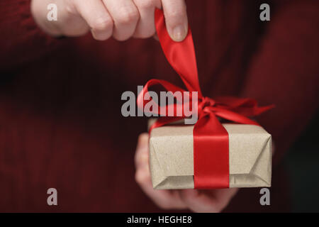 Femmina mani teen apre imbarcazioni carta regalo con fiocco rosso Foto Stock